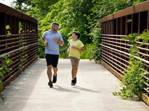Father and son jogging together on a wooden bridge surrounded by lush greenery