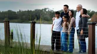 Family of six smiling and standing together by a lakeside railing, looking off to the side