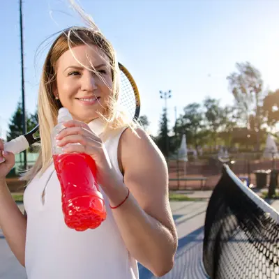 A young woman holding an energy drink and a tennis racquet. 