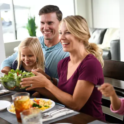 Family of four smiling and sharing a meal together at the dining table.