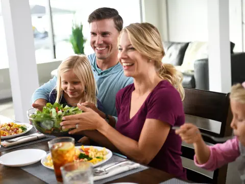 Family of four smiling and sharing a meal together at the dining table.