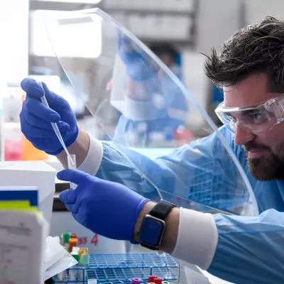 Scientist in lab coat and protective gear working with pipette, showcasing safety and precision in research.
