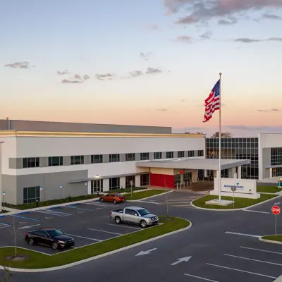 Aerial view of AdventHealth hospital with cars parked, an American flag, and a clear sky at sunset.