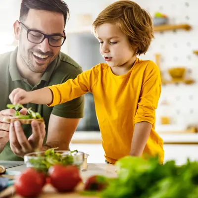 Happy father and son cooperating while making a sandwich in the kitchen.
