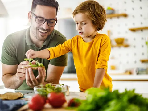 Happy father and son cooperating while making a sandwich in the kitchen.