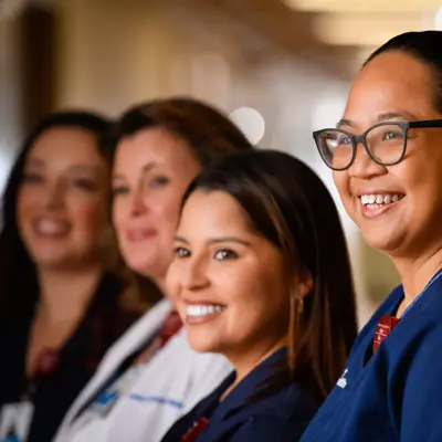 Group of smiling nurses in scrubs standing together in a healthcare facility hallway