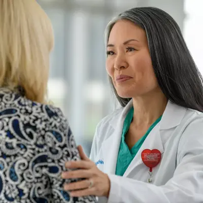 A doctor in a white coat and green shirt talks to a patient in a blue and white patterned shirt.