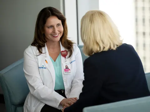 A smiling doctor in a white coat talks to a patient in a medical office.