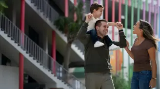 A child riding on his fathers shoulders while his smiling mother walks along side.
