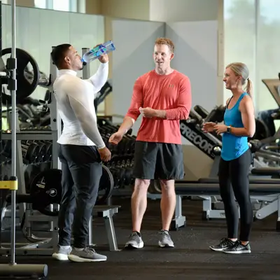 Three people in a gym, one drinking water, engaging in conversation.