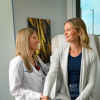 A smiling doctor in a lab coat holds the hand of a smiling patient in a clinic.