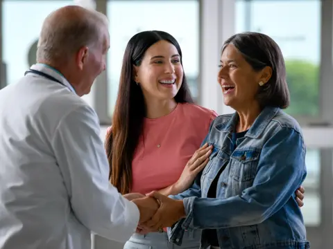 A doctor shakes hands with two smiling women, conveying a positive and engaging atmosphere.
