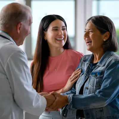 A doctor shakes hands with two smiling women, conveying a positive and engaging atmosphere.