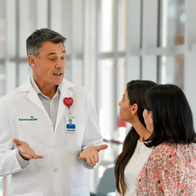 A doctor in a white coat speaks with two women in a hospital corridor.