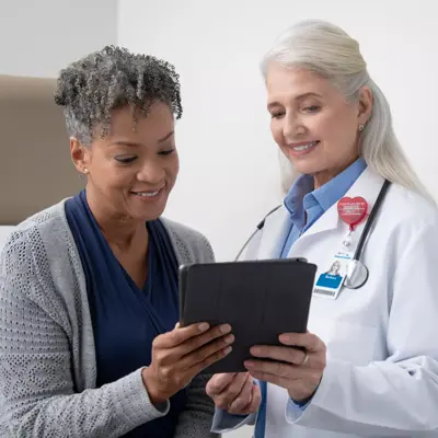 A smiling doctor shows a patient information on a tablet in a medical setting.