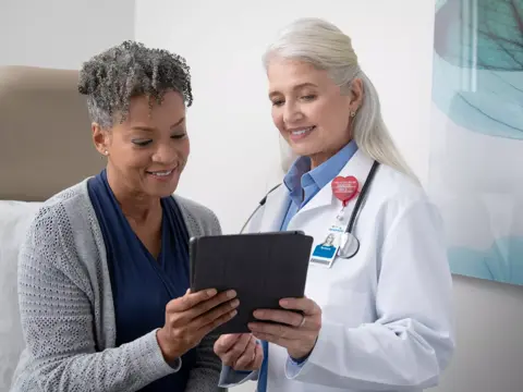 A smiling doctor shows a patient information on a tablet in a medical setting.