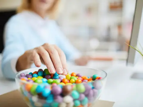 A hand reaching for a bowl of candy.
