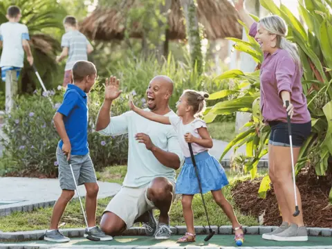 A family of four enjoys a fun day at the mini-golf course, with smiles and laughter.