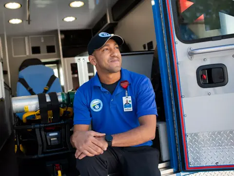 A smiling emergency medical technician sits inside an ambulance, ready for service.