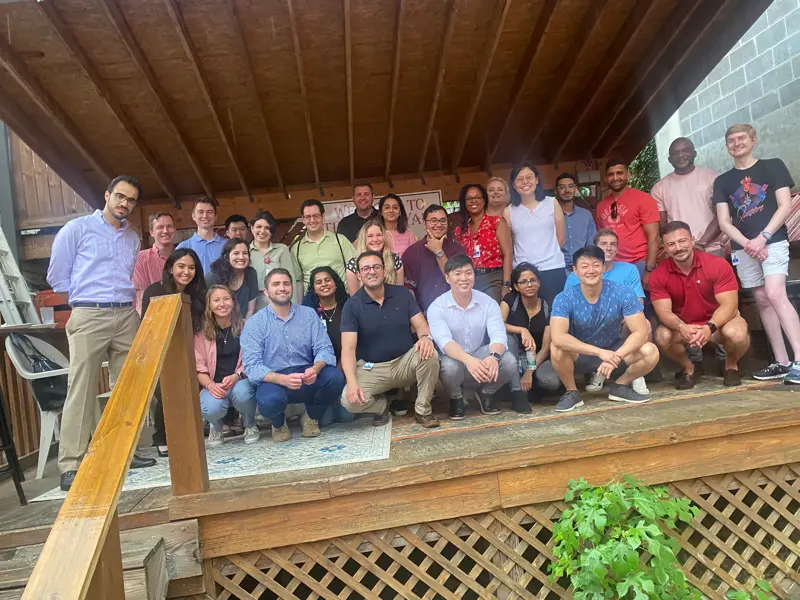 Large group smiling and posing on a wooden deck under a covered patio.