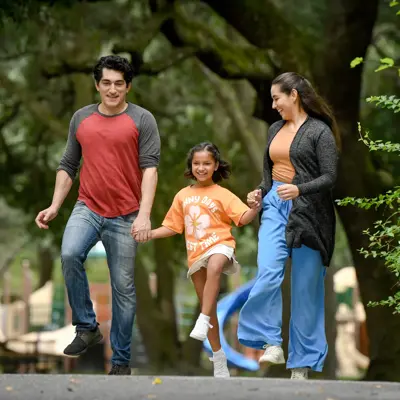 A family of three walks together in a park, smiling and holding hands.