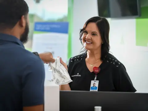 A smiling woman in a black shirt hands a white cloth to a man in a blue shirt.