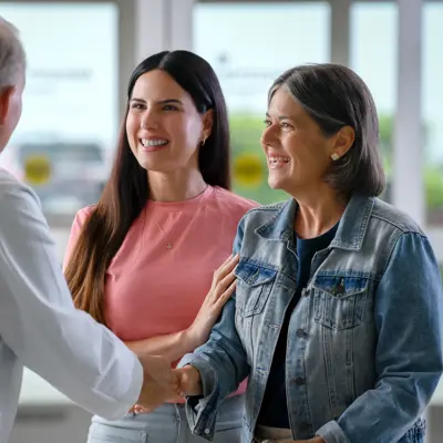 A doctor shakes hands with two smiling women, fostering a warm and engaging atmosphere.