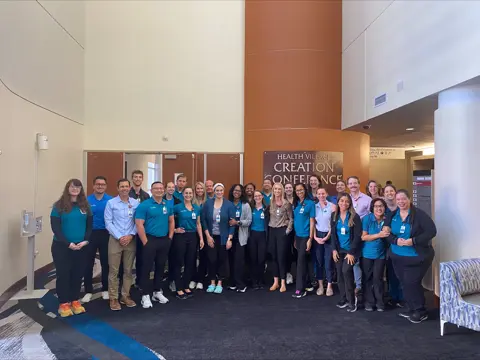 Large group poses together in front of a conference center sign.