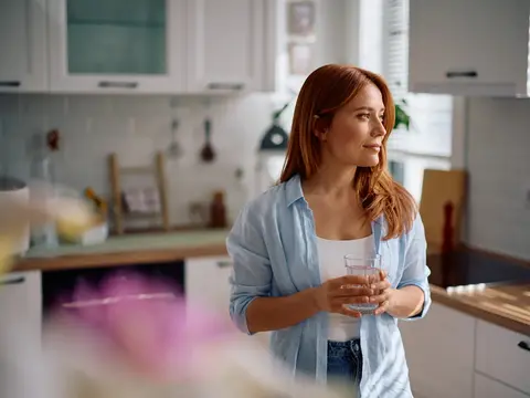 Pensive woman with glass of water in the kitchen.