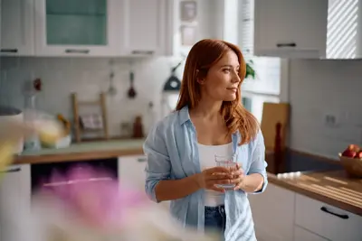 Pensive woman with glass of water in the kitchen.
