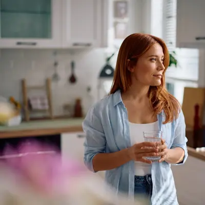 Pensive woman with glass of water in the kitchen.