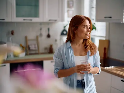 Pensive woman with glass of water in the kitchen.