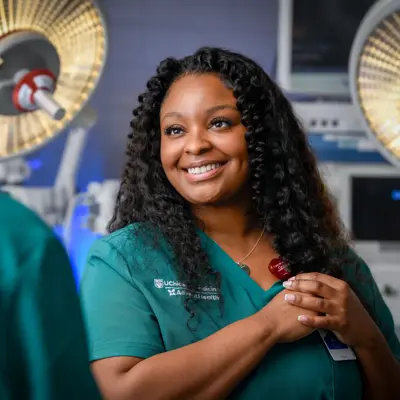 Smiling healthcare professional in teal scrubs standing in an operating room with surgical lights visible in the background