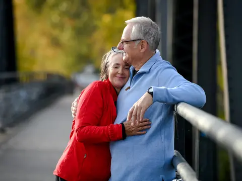 An elderly couple embracing on a bridge, showcasing warmth and connection.