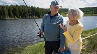 Elderly couple fishing by the lake, man holding rod, woman holding tackle box.