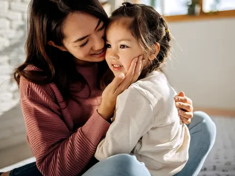 A young woman holding her little girl and smiling.