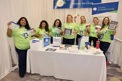 AdventHealth team members at a Stroke Services booth displaying stroke warning signs and educational materials at a women’s health event.