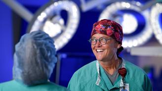 Smiling female surgeon in scrubs and surgical cap stands in operating room.