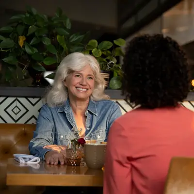 Two women sit at a table in a restaurant, smiling and conversing.