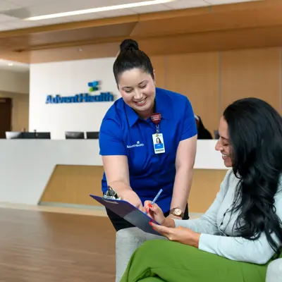 A smiling AdventHealth employee assists a patient, reviewing documents together in a welcoming lobby.