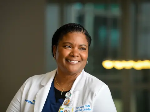 Portrait of Tammy BSN, a smiling nurse leader at AdventHealth, wearing a white lab coat and name tag.