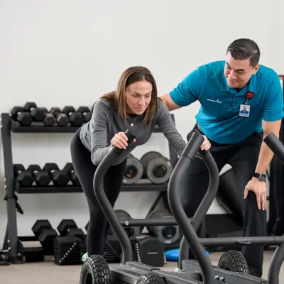 A woman and a man in a gym using a workout machine together.