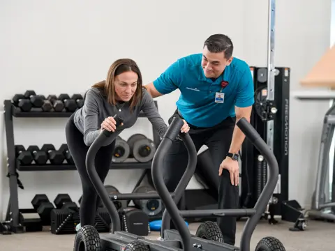A woman and a man in a gym using a workout machine together.