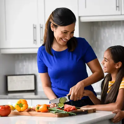 Mother in blue shirt preparing vegetables with two young daughters in a bright modern kitchen