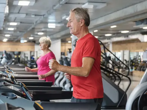 Older man and woman exercising on treadmills at a fitness center.