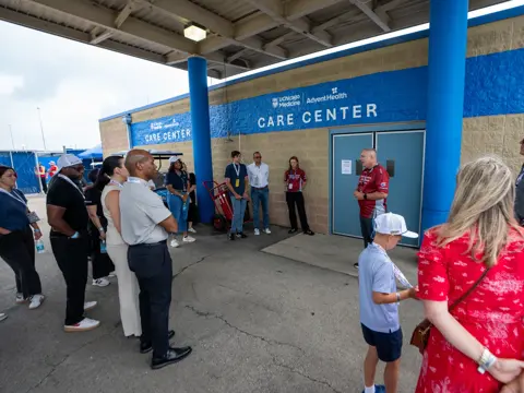 Group of people gather outside a care center entrance, listening to a speaker beneath signage for UChicago Medicine and AdventHealth.