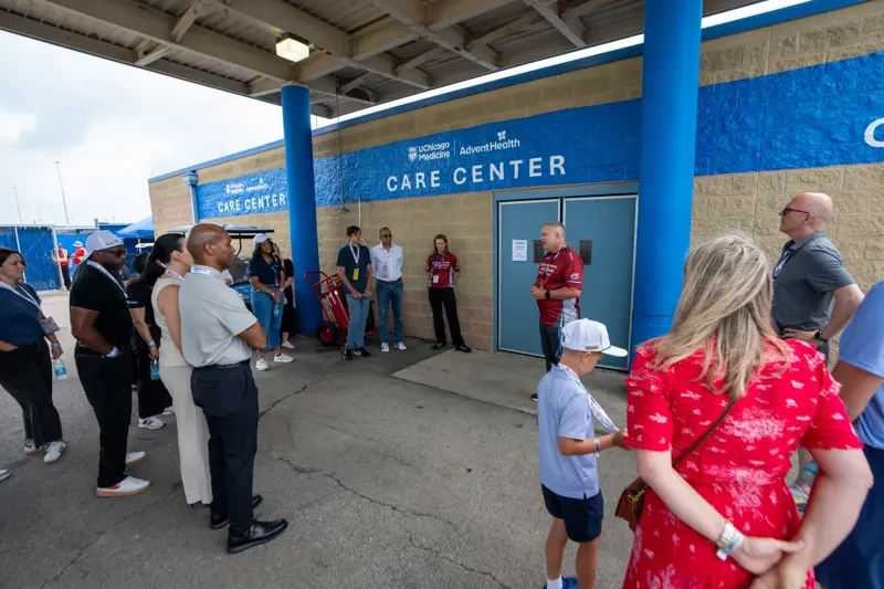 Group of people gather outside a care center entrance, listening to a speaker beneath signage for UChicago Medicine and AdventHealth.