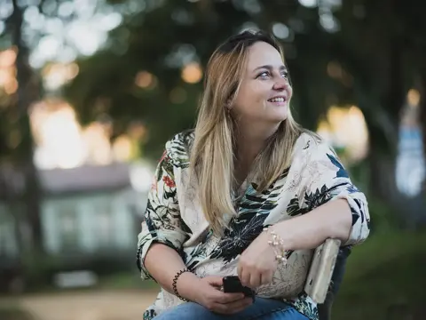 Smiling woman sitting outdoors on a park bench and looking to the side.