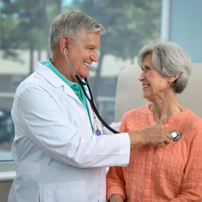 Doctor in white coat with stethoscope examining a smiling female patient in a coral shirt in a bright medical facility