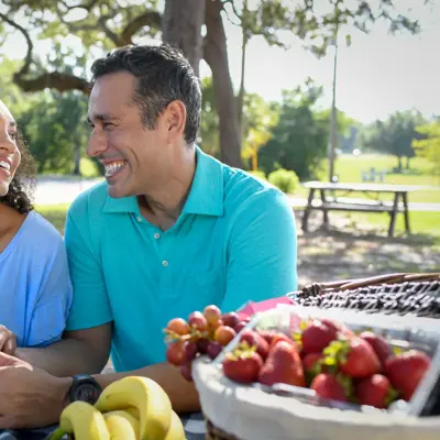 A smiling couple enjoying a picnic with fruit, showcasing a warm and engaging atmosphere.
